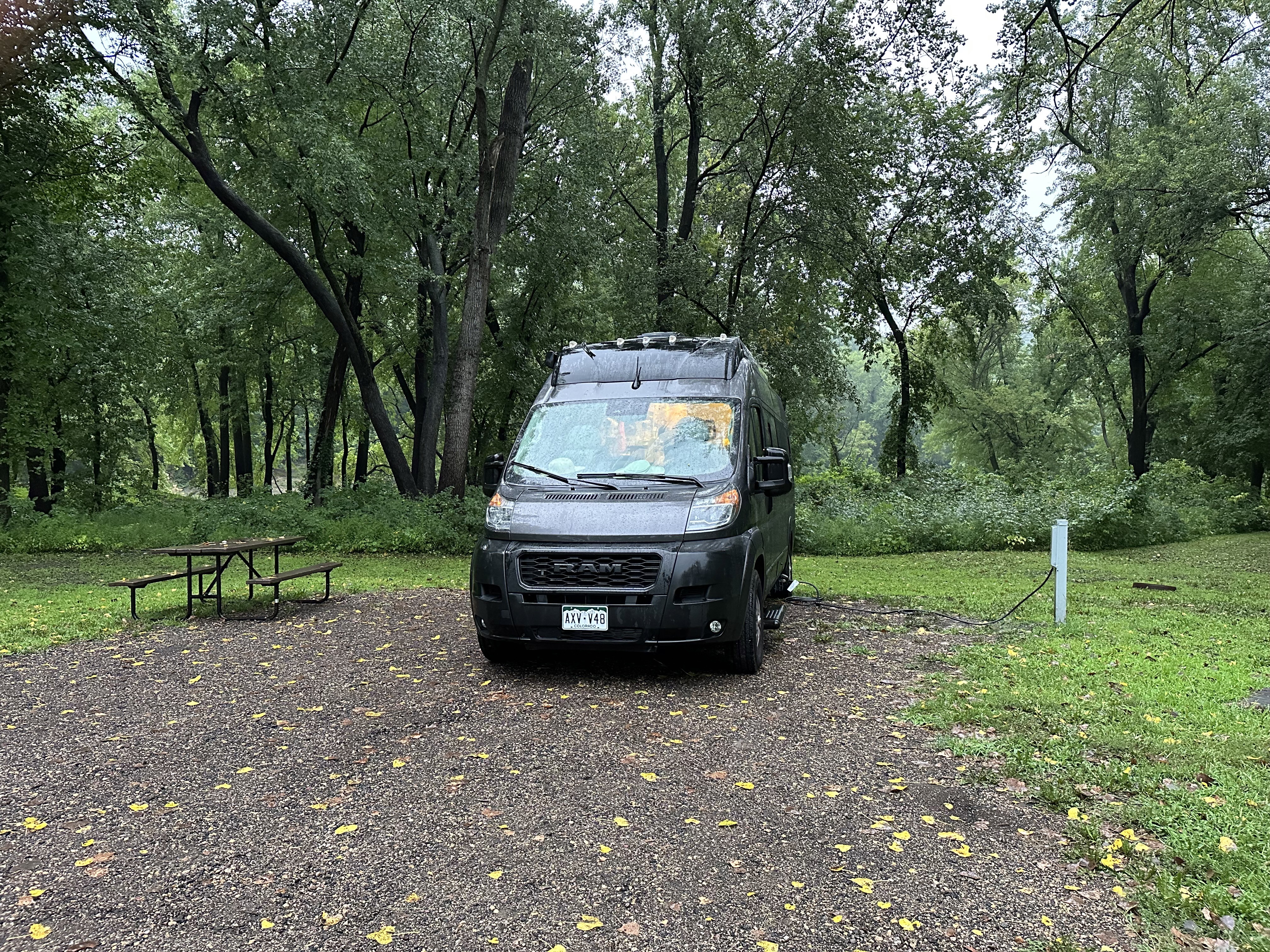 Vandy Patinkin parked on a gravel site with a picnic table surrounded by grass and with bushes and trees in the background