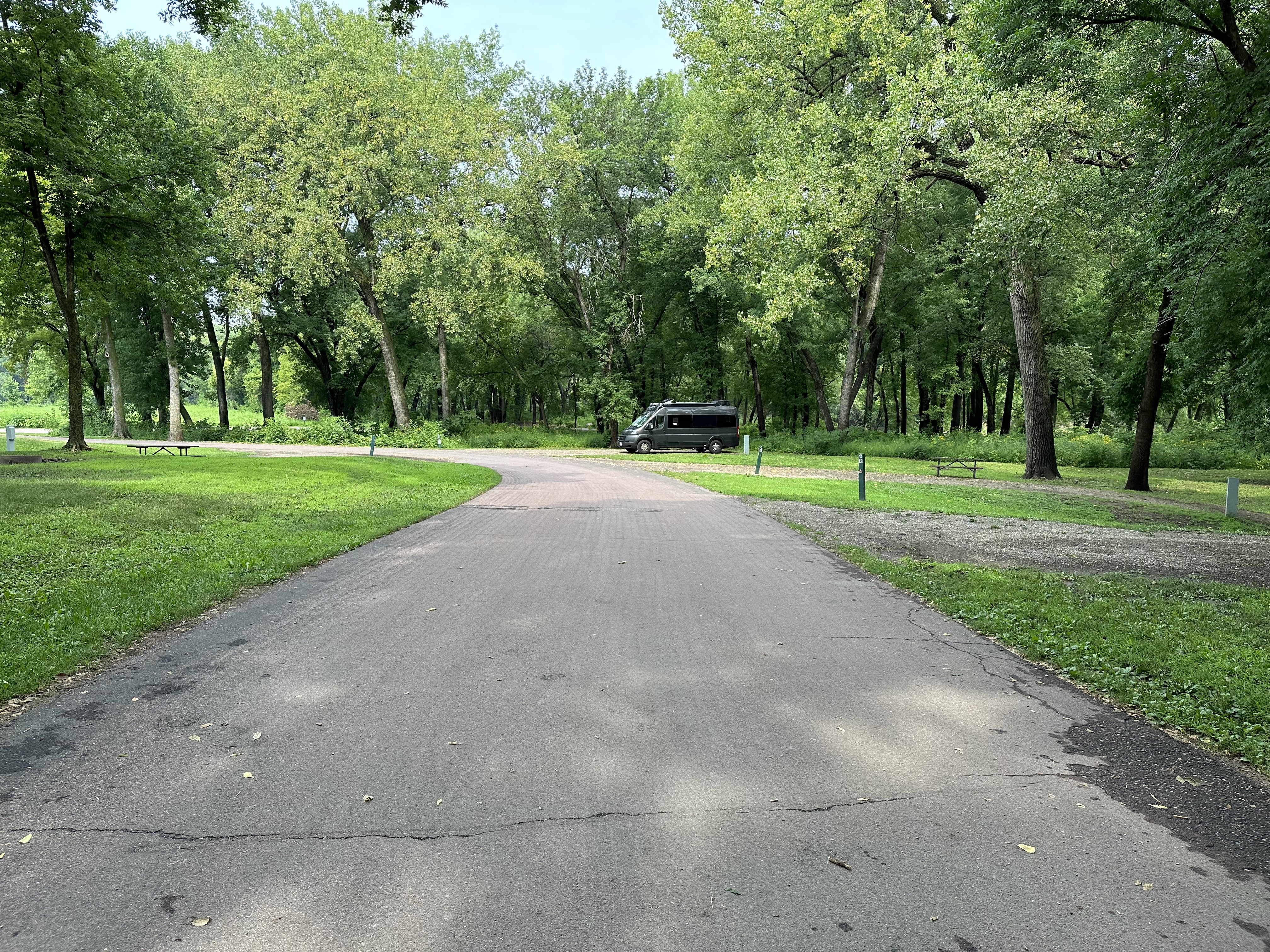 Vandy Patinkin in the distance parked in a gravel spot surrounded by tall trees